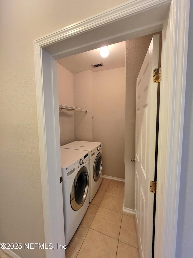 washroom with laundry area, visible vents, light tile patterned flooring, washing machine and clothes dryer, and baseboards