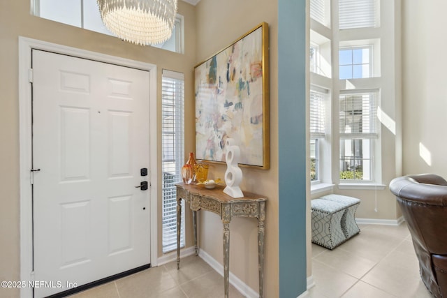 foyer with a towering ceiling, tile patterned flooring, a notable chandelier, and baseboards