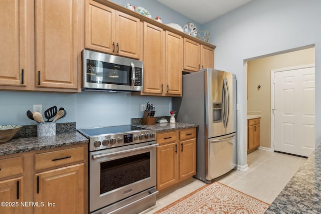 kitchen with light tile patterned flooring, dark stone countertops, brown cabinets, and stainless steel appliances