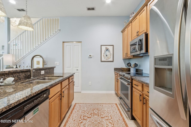 kitchen featuring dark stone countertops, a sink, visible vents, stainless steel appliances, and decorative light fixtures
