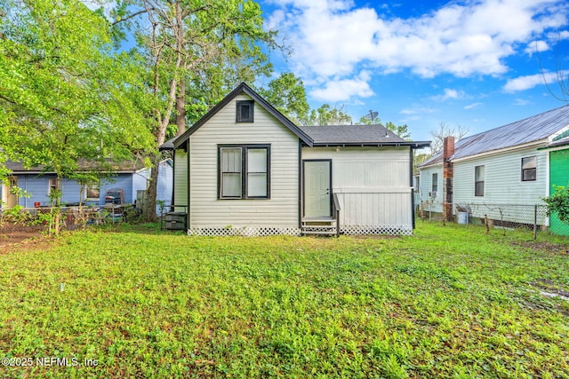 back of house featuring entry steps, fence, roof with shingles, and a lawn