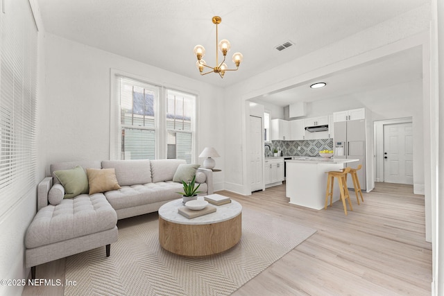 living room featuring a notable chandelier, visible vents, baseboards, and light wood-style flooring