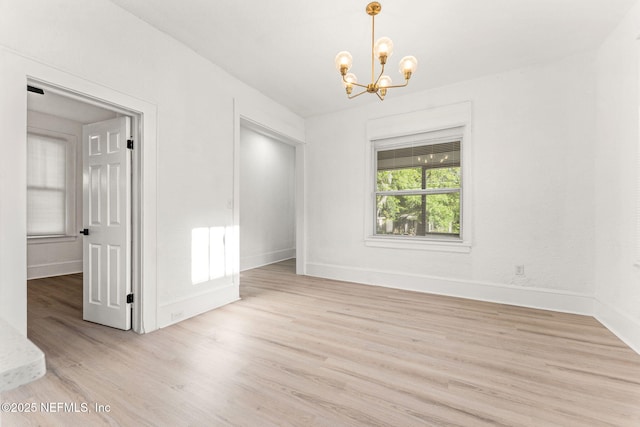 empty room featuring light wood-style floors, a notable chandelier, and baseboards