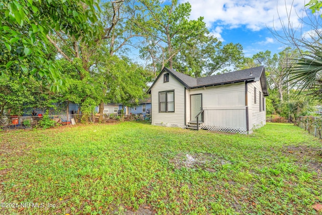 back of property featuring a shingled roof, entry steps, a fenced backyard, and a lawn