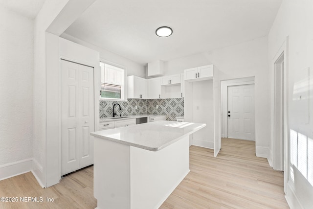 kitchen with tasteful backsplash, light wood-type flooring, white cabinets, a center island, and a sink
