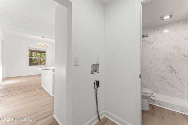 bathroom featuring toilet, a stall shower, wood finished floors, and a notable chandelier