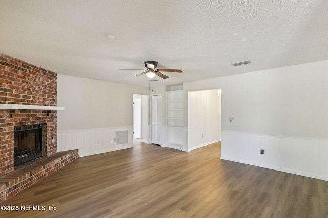 2566 Sandlewood Cir, Orange Park, FL 32065 - unfurnished living room with a fireplace, a textured ceiling, a ceiling fan, a wainscoted wall, and wood finished floors