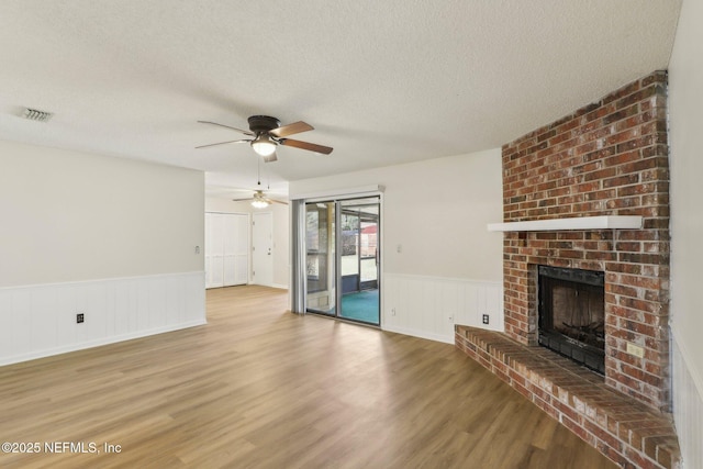 2566 Sandlewood Cir, Orange Park, FL 32065 - unfurnished living room with ceiling fan, a textured ceiling, a fireplace, wood finished floors, and a wainscoted wall