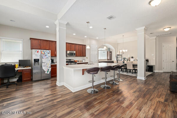 kitchen featuring a kitchen bar, ornate columns, appliances with stainless steel finishes, and light countertops