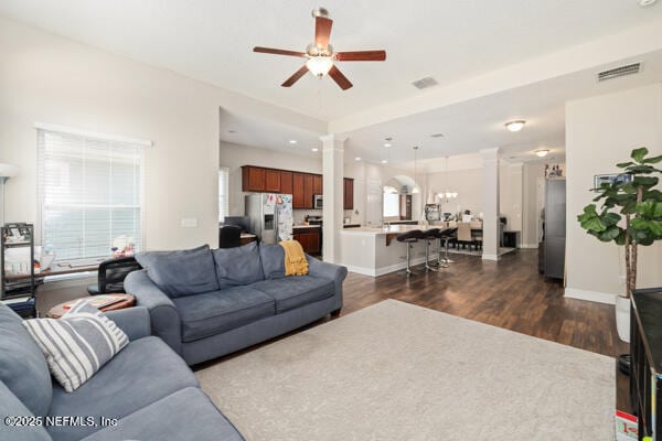 living room featuring baseboards, dark wood-type flooring, visible vents, ceiling fan, and decorative columns