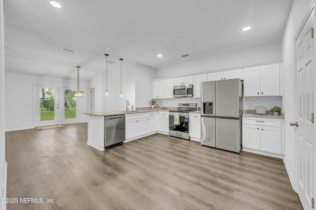 kitchen with stainless steel appliances, a peninsula, a sink, and light wood finished floors