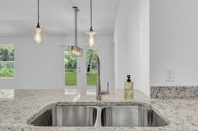 interior details with pendant lighting, a sink, and light stone countertops