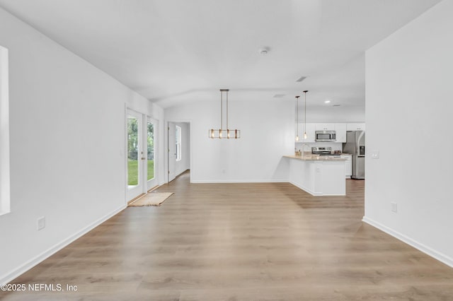 unfurnished living room with baseboards, light wood-type flooring, an inviting chandelier, and lofted ceiling