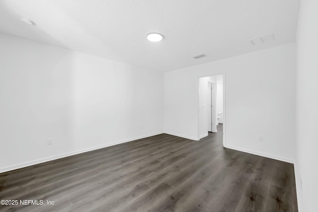 empty room featuring dark wood-style floors, baseboards, and visible vents