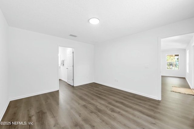 empty room featuring dark wood-style flooring, baseboards, and visible vents