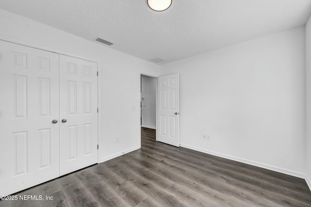 unfurnished bedroom with a textured ceiling, a closet, visible vents, baseboards, and dark wood-style floors