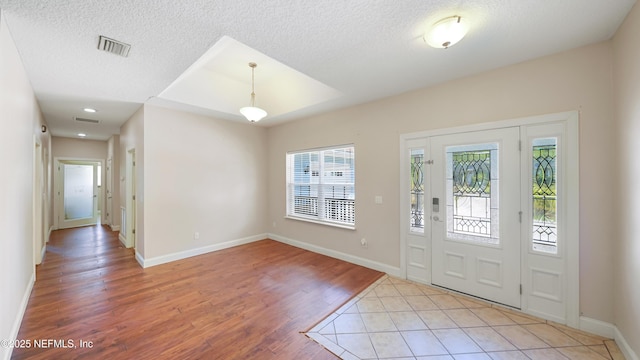 foyer entrance with light wood-type flooring, baseboards, visible vents, and a textured ceiling