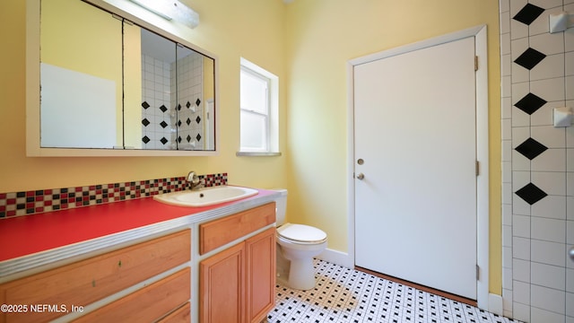 full bathroom featuring vanity, baseboards, a tile shower, and toilet