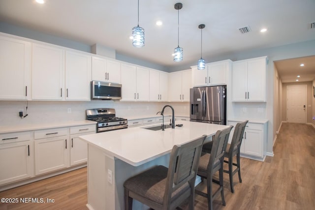 kitchen with light wood-type flooring, white cabinets, visible vents, stainless steel appliances, and a sink