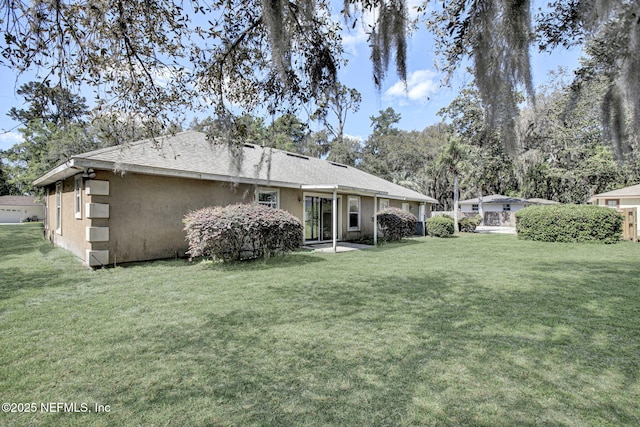 rear view of property with a shingled roof, stucco siding, and a lawn
