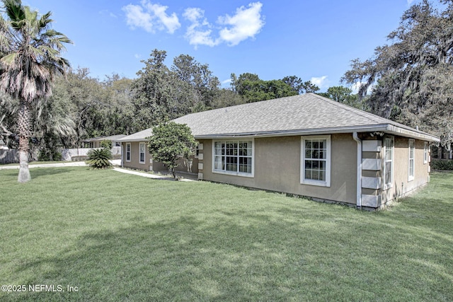 rear view of house featuring a shingled roof, a lawn, and stucco siding