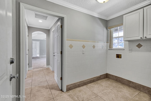 bathroom featuring a textured ceiling, ornamental molding, tile patterned flooring, visible vents, and tile walls