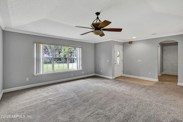 carpeted spare room featuring crown molding, ceiling fan, arched walkways, a textured ceiling, and baseboards