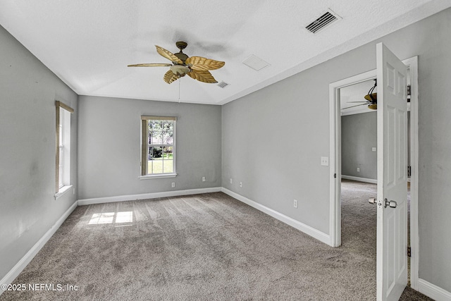 carpeted empty room with visible vents, ceiling fan, and baseboards