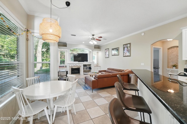 13738 Harbor Creek Pl, Jacksonville, FL 32224 - dining room with ceiling fan, light tile patterned floors, arched walkways, ornamental molding, and a glass covered fireplace