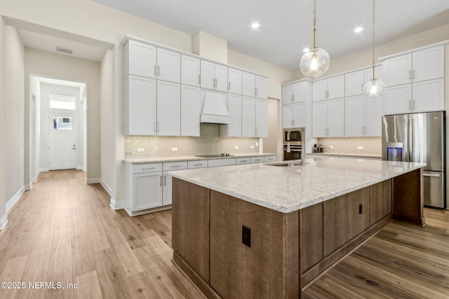 kitchen with backsplash, white cabinets, premium range hood, and stainless steel appliances