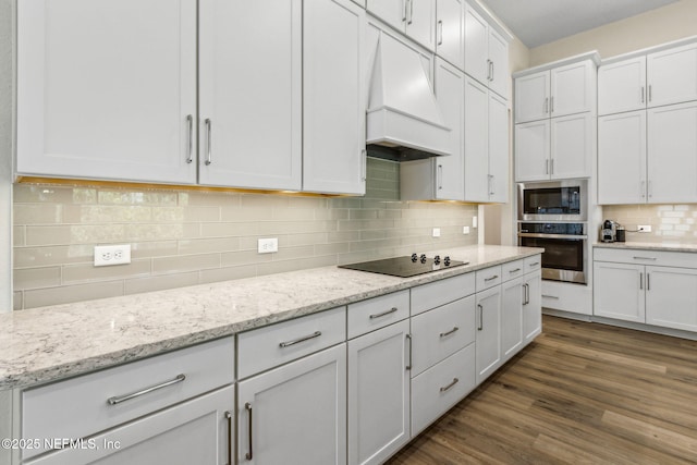 kitchen featuring tasteful backsplash, white cabinets, appliances with stainless steel finishes, wood finished floors, and custom range hood
