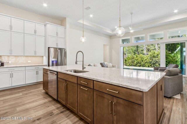 kitchen featuring a raised ceiling, a sink, open floor plan, stainless steel appliances, and backsplash