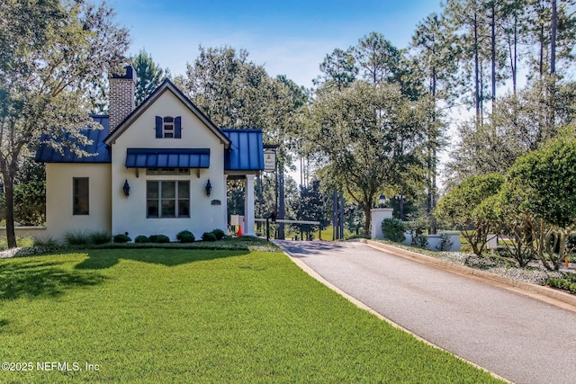 view of front of house featuring aphalt driveway, stucco siding, a chimney, and a front lawn