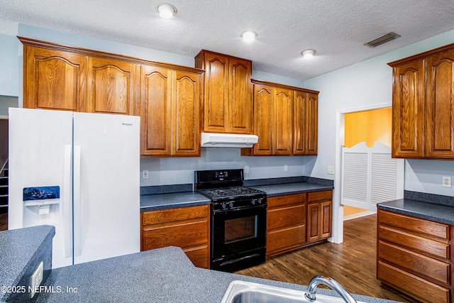 kitchen with white refrigerator with ice dispenser, black gas stove, dark countertops, and under cabinet range hood