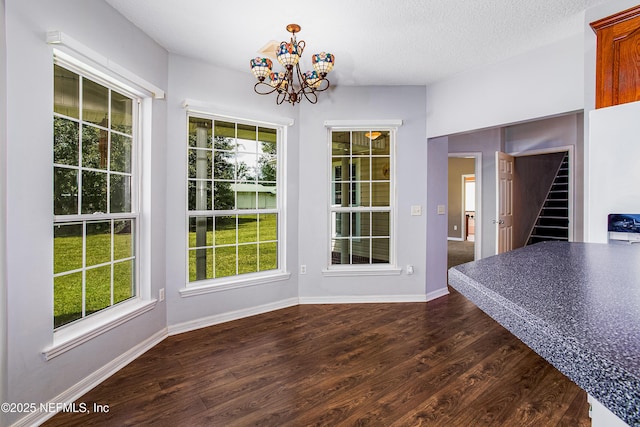 unfurnished dining area with baseboards, a chandelier, a textured ceiling, stairway, and dark wood-type flooring