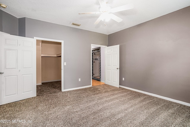 unfurnished bedroom featuring visible vents, baseboards, a textured ceiling, a walk in closet, and carpet flooring