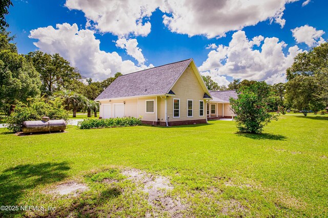 rear view of property featuring roof with shingles, a yard, and a garage