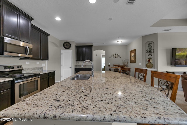 kitchen with arched walkways, a spacious island, a sink, light stone counters, and stainless steel appliances