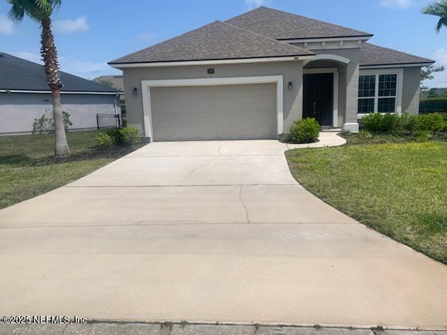 view of front of house with an attached garage, a shingled roof, stucco siding, and a front yard