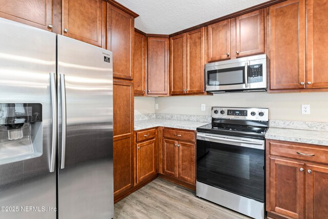 kitchen featuring brown cabinetry, light wood-type flooring, light countertops, a textured ceiling, and appliances with stainless steel finishes