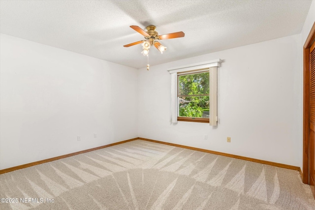 carpeted empty room with a textured ceiling, baseboards, and a ceiling fan
