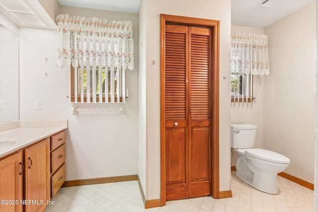 bathroom with a closet, baseboards, toilet, vanity, and wallpapered walls