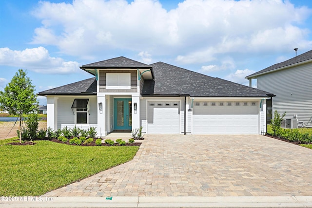view of front facade with central air condition unit, decorative driveway, roof with shingles, a front lawn, and an attached garage
