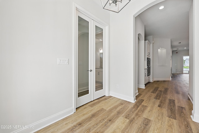 hallway with arched walkways, french doors, light wood-type flooring, and baseboards