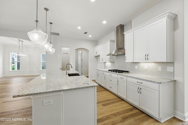 kitchen featuring wall chimney exhaust hood, light wood-type flooring, white cabinetry, a sink, and decorative backsplash