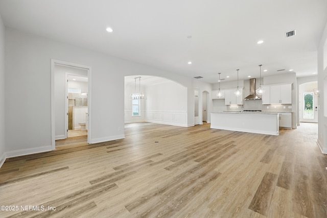 unfurnished living room featuring recessed lighting, arched walkways, visible vents, and light wood-type flooring
