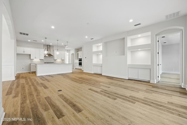 unfurnished living room featuring light wood-style floors, arched walkways, visible vents, and recessed lighting