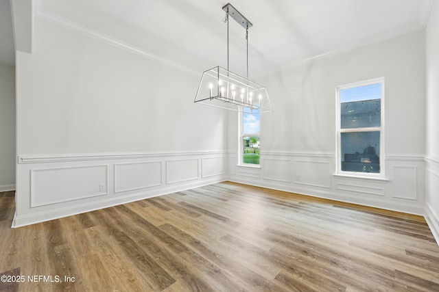 unfurnished dining area with a notable chandelier, crown molding, and wood finished floors