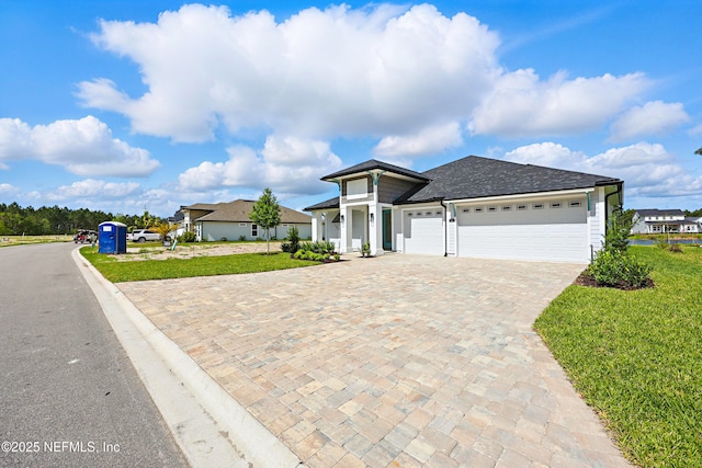 view of front of property with an attached garage, roof with shingles, a front lawn, and decorative driveway