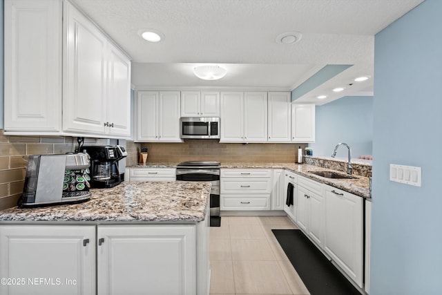 275 1st St S Unit 504, Jacksonville Beach, FL 32250 - kitchen with a sink, appliances with stainless steel finishes, white cabinets, decorative backsplash, and light stone counters